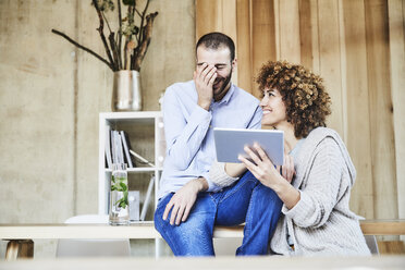 Glücklicher Mann und Frau teilen sich ein Tablet in einem modernen Büro - FMKF05553