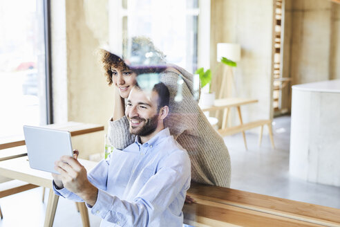 Lächelnder Mann und Frau teilen sich ein Tablet in einem modernen Büro - FMKF05556