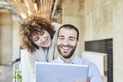 Glücklicher Mann und Frau teilen sich ein Tablet in einem modernen Büro - FMKF05557