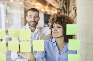 Two colleagues brainstorming with post-its on glass pane - FMKF05561