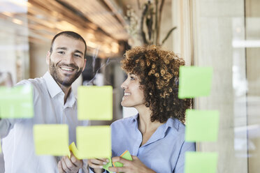 Zwei glückliche Kollegen beim Brainstorming mit Post-its auf einer Glasscheibe - FMKF05563