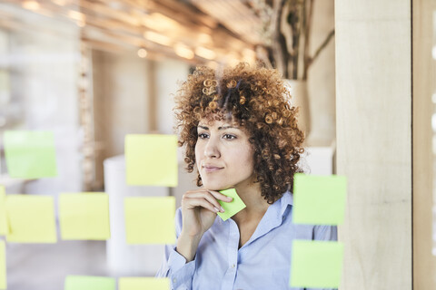 geschäftsfrau beim Brainstorming mit Post-its auf Glasscheibe, lizenzfreies Stockfoto