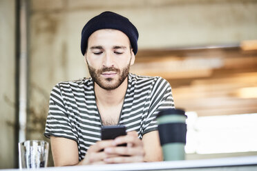 Junger Mann mit Mütze und Mobiltelefon - FMKF05570