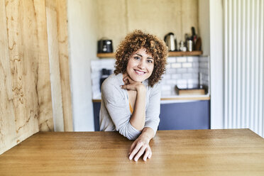 Porträt einer lächelnden Frau, die sich auf einen Holztisch stützt - FMKF05579