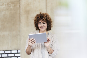 Smiling woman using tablet at concrete wall - FMKF05599