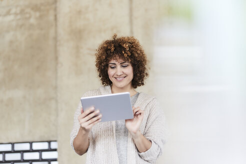 Lächelnde Frau mit Tablet an einer Betonwand - FMKF05599