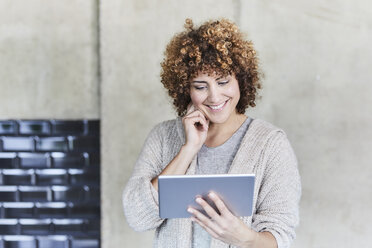 Lächelnde Frau mit Tablet an einer Betonwand - FMKF05606