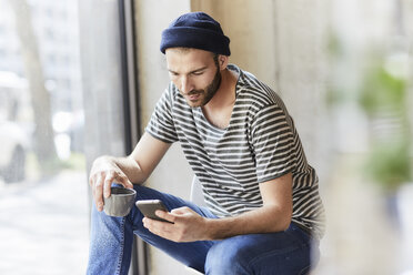 Young man holding coffee cup using cell phone - FMKF05607