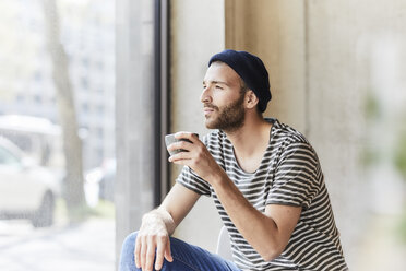 Junger Mann hält Kaffeetasse am Fenster - FMKF05608