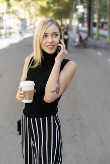 Porträt einer lächelnden blonden Frau mit Kaffee zum Mitnehmen beim Telefonieren - GIOF06216