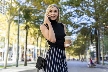 Porträt einer lächelnden blonden Frau mit Kaffee zum Mitnehmen beim Telefonieren - GIOF06217