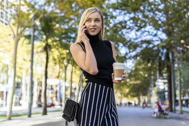 Portrait of smiling blond woman with coffee to go on the phone - GIOF06217