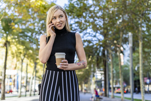 Porträt einer lächelnden blonden Frau mit Kaffee zum Mitnehmen beim Telefonieren - GIOF06218