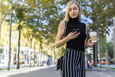 Porträt einer blonden Frau mit Kaffee zum Mitnehmen, die auf ihr Mobiltelefon schaut - GIOF06219