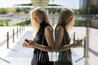 Blond young woman with coffee to go looking at cell phone - GIOF06239