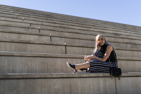 Blonde junge Frau am Telefon auf einer Treppe im Freien sitzend, lizenzfreies Stockfoto