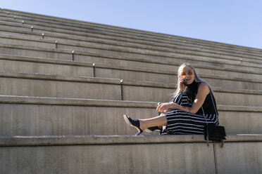 Blonde junge Frau am Telefon auf einer Treppe im Freien sitzend - GIOF06242