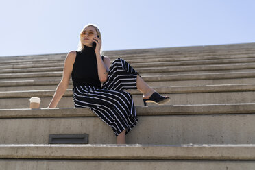 Blond young woman on the phone sitting on stairs outdoors - GIOF06243