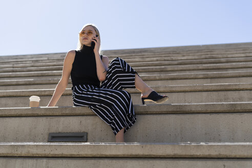 Blonde junge Frau am Telefon auf einer Treppe im Freien sitzend - GIOF06243