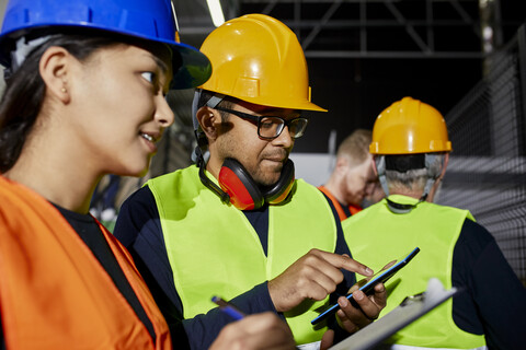 Male and female worker with clipboard and tablet talking in factory stock photo