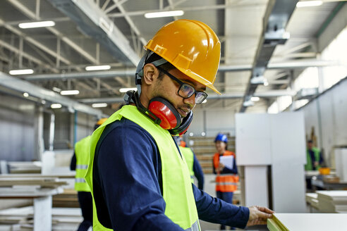 Arbeiter, der ein Holzbrett in einer Fabrik untersucht - ZEDF02097