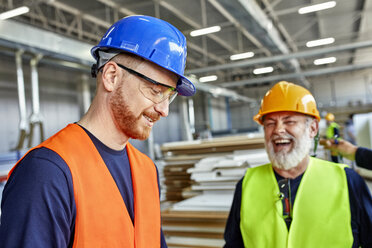 Happy colleagues in protective workwear talking in factory - ZEDF02105