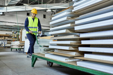 Worker pulling pallet jack with wooden boards in factory - ZEDF02119