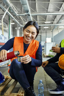 Glückliche Arbeiterin gießt während der Mittagspause in einer Fabrik ein Getränk in einen Becher - ZEDF02133