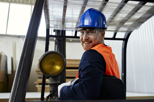 Porträt eines lächelnden Arbeiters auf einem Gabelstapler in einer Fabrik - ZEDF02148