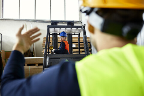 Arbeiter, der einem Mann auf einem Gabelstapler in einer Fabrik hilft, lizenzfreies Stockfoto