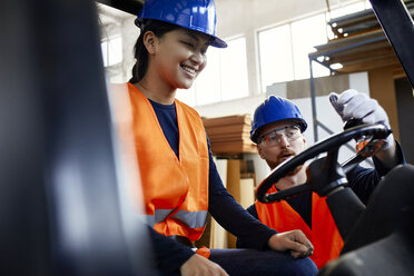 Man instructing female worker on forklift in factory - ZEDF02154