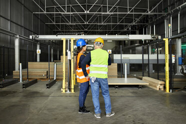 Rear view of male and female worker standing in factory workshop - ZEDF02179