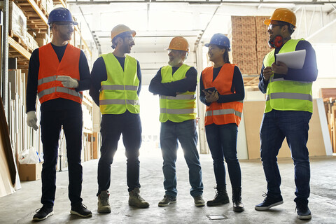 Lächelnde Arbeiter stehen in einer Fabrikhalle und unterhalten sich, lizenzfreies Stockfoto