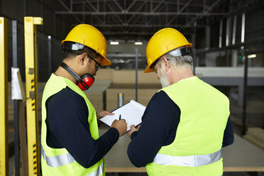 Two men signing document in factory warehouse - ZEDF02191