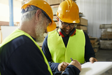 Zwei Männer unterzeichnen ein Dokument in einem Fabriklager - ZEDF02192