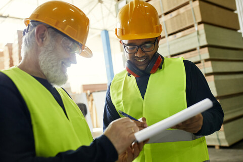 Zwei lächelnde Männer unterzeichnen ein Dokument in einem Fabriklager, lizenzfreies Stockfoto