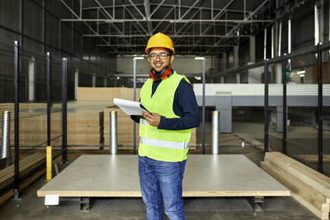 Porträt eines lächelnden Arbeiters mit Zwischenablage in einem Fabriklager, lizenzfreies Stockfoto