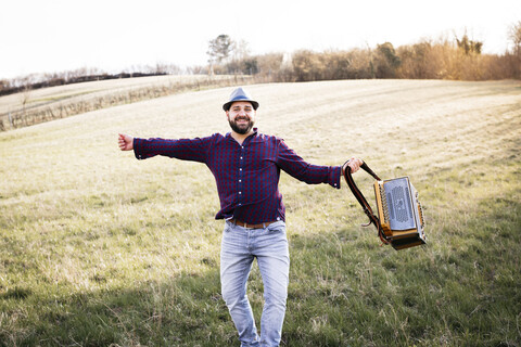 Bärtiger Mann mit Akkordeon tanzt auf einer Wiese, lizenzfreies Stockfoto