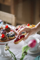 Woman's hand putting Eclair on cake stand - ALBF00865