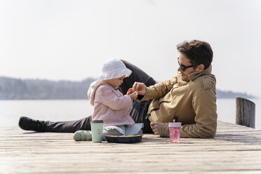 Germany, Bavaria, Herrsching, father and daughter relaxing on jetty having a snack - DIGF06738