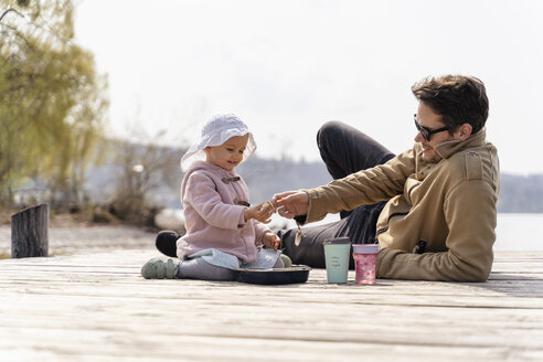 Germany, Bavaria, Herrsching, father and daughter relaxing on jetty having a snack - DIGF06739