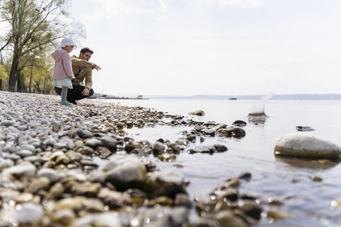 Deutschland, Bayern, Herrsching, Vater und Tochter am Kieselstrand am Seeufer - DIGF06740