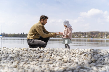 Germany, Bavaria, Herrsching, father and daughter on pebble beach at lakeshore - DIGF06741
