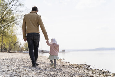 Germany, Bavaria, Herrsching, father and daughter walking on pebble beach at lakeshore - DIGF06742