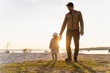 Germany, Bavaria, Herrsching, father and daughter walking at the lakeshore at sunset - DIGF06744