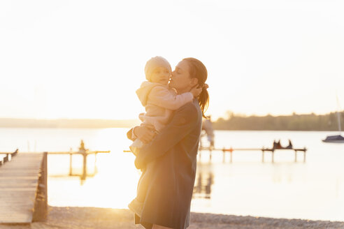 Germany, Bavaria, Herrsching, mother carrying daughter at the lakeshore at sunset - DIGF06747