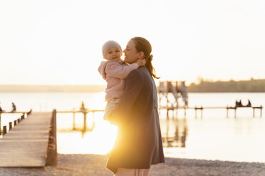 Deutschland, Bayern, Herrsching, Mutter trägt Tochter am Seeufer bei Sonnenuntergang - DIGF06748