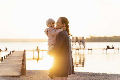 Germany, Bavaria, Herrsching, mother carrying daughter at the lakeshore at sunset - DIGF06748