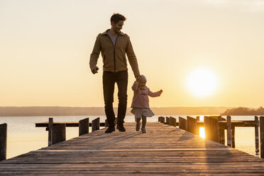 Germany, Bavaria, Herrsching, father and daughter walking on jetty at sunset - DIGF06752