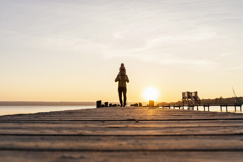 Deutschland, Bayern, Herrsching, Vater trägt Tochter auf Schultern auf Steg bei Sonnenuntergang, lizenzfreies Stockfoto